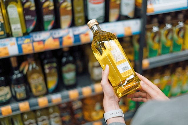 A close-up image of a person holding a bottle of olive oil in the grocery store