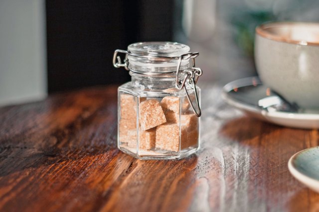 An image of a clear condiment shaker with brown sugar cubes near a gray teacup

