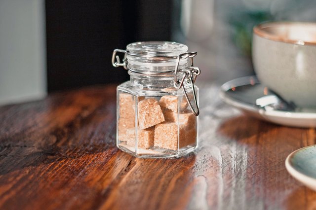 An image of a clear condiment shaker with brown sugar cubes near a gray teacup