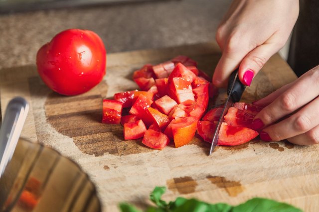 An image of tomatoes being cut on a wooden cutting board