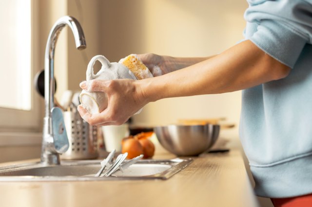 A person with rolled up sleeves washes dishes at the sink