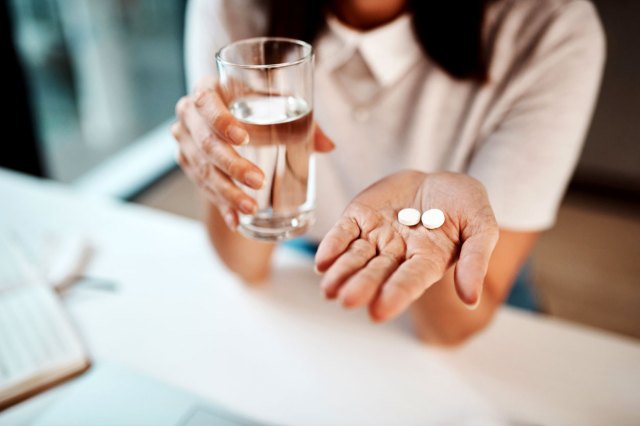 An image of a woman holding a glass of water and two white pills
