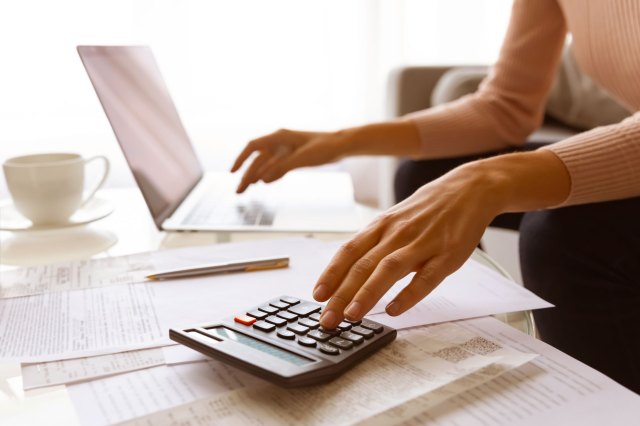 A woman types on a laptop and a calculator at the same time