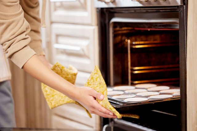 A woman slides a tray of cookies out of the oven