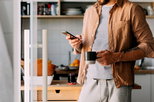 An image of a man looking at his phone while holding a mug in a kitchen