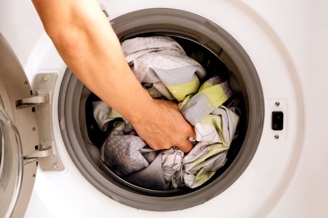A close-up image of a person putting sheets into the dryer