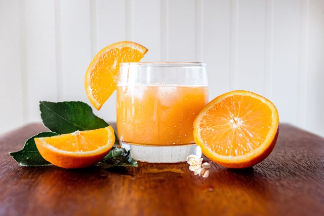An image of a glass of orange juice and oranges on a wooden table