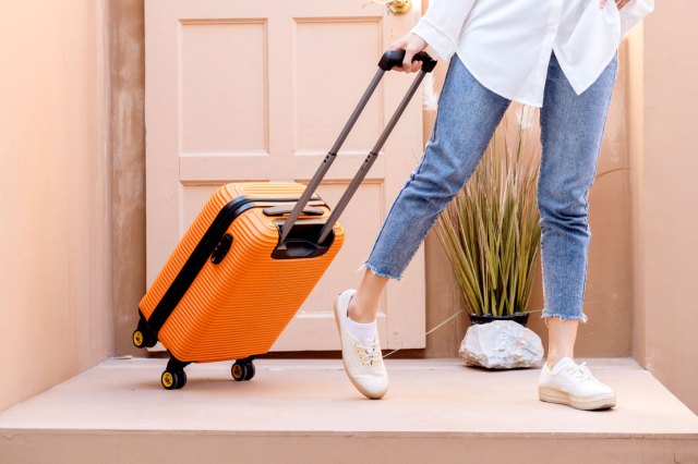Woman in jeans pulls an orange suitcase on a house landing