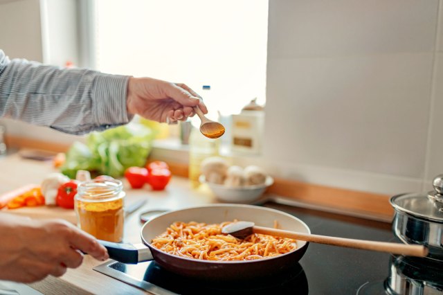 An image of a person adding spices to a pan of food on the stove