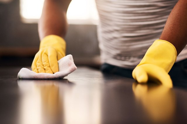 A close-up image of a person in yellow rubber gloves wiping a counter