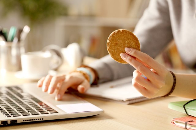 An image of a person at a computer and holding a cookie