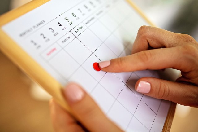 A close-up image of a person putting a red dot sticker on a calendar