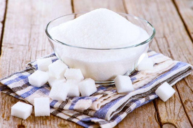 An image of a bowl of sugar surrounded by sugar cubes on a wooden table