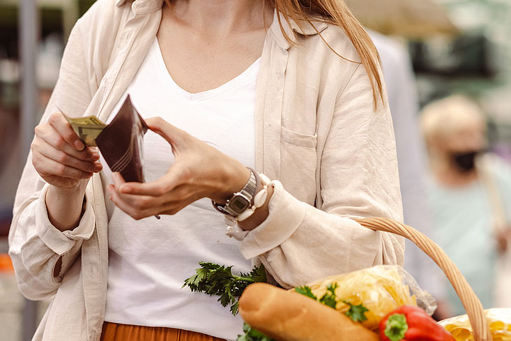 Woman takes cash out of wallet while holding a wicker basket full of groceries