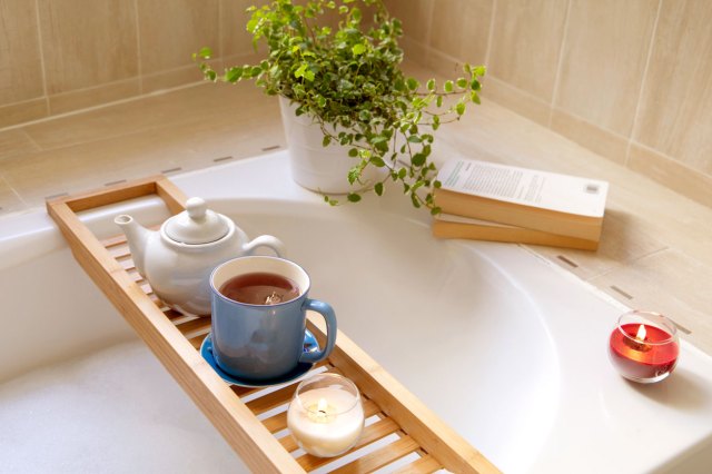 A bath setup including a tray for drinks, a plant, a book, and a candle