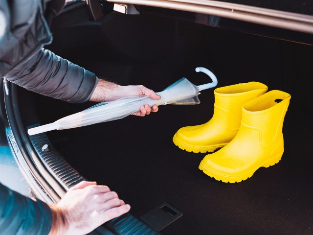 An image of a man putting an umbrella in the trunk of a car that contains yellow rain boots