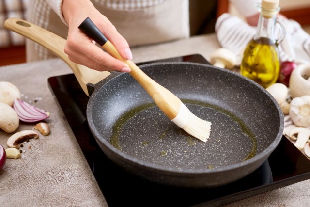 A close-up image of a person brushing oil into a pan on a burner