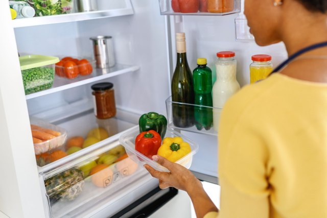 A woman prepares to put a container of bell peppers into the refrigerator