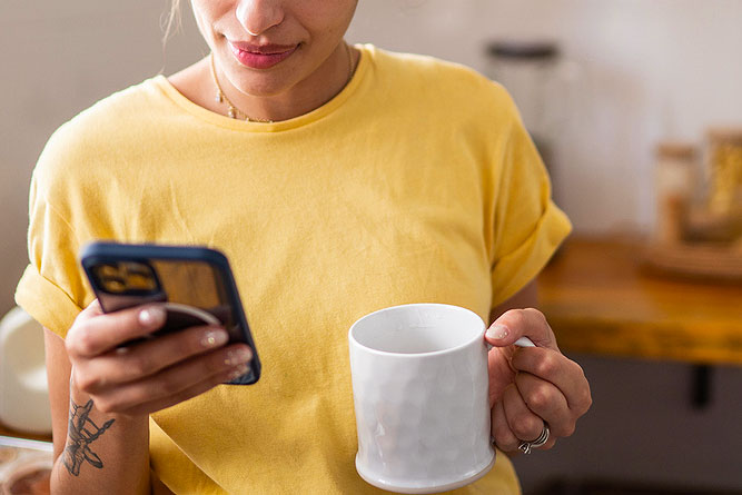 An image of a woman holding a white coffee mug looking at her phone