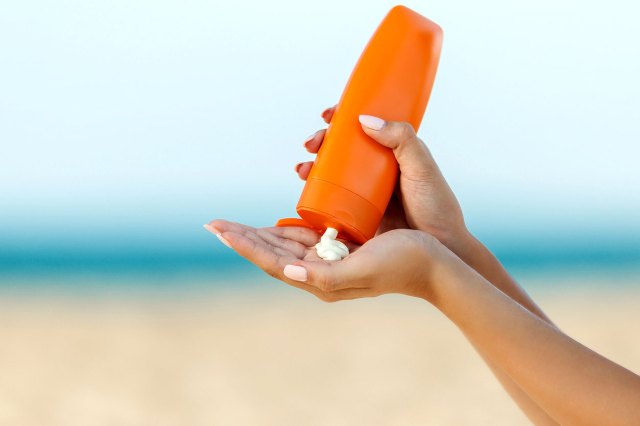 A close-up image of a person squeezing sunscreen from an orange bottle into their hand