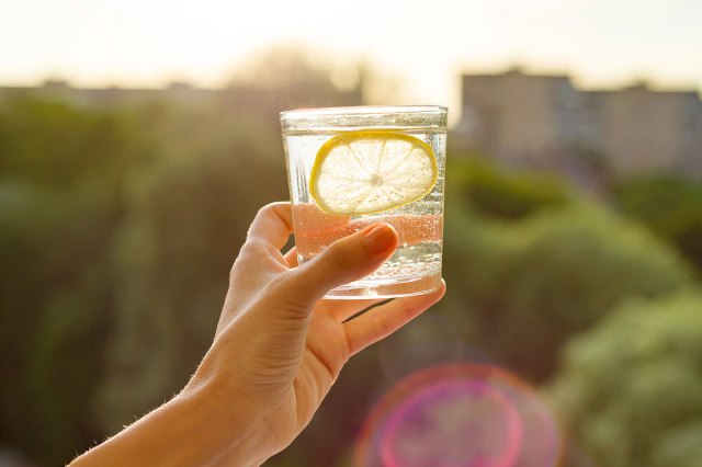 An image of a handing holding a glass of water with a lemon up in the air