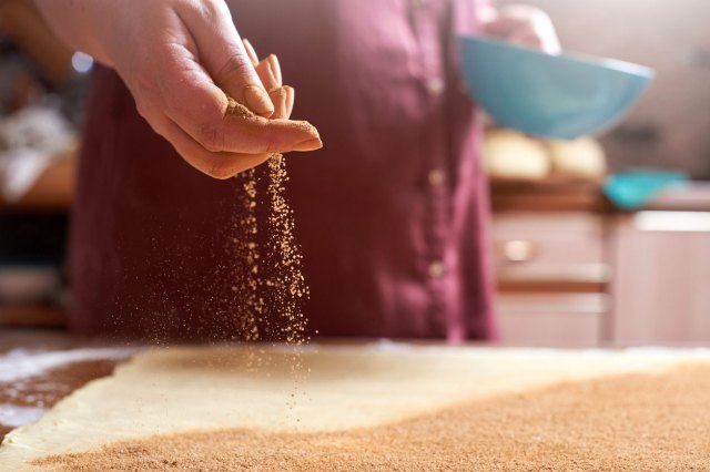An image of someone sprinkling spices onto a table as they hold a blue bowl in the other hand