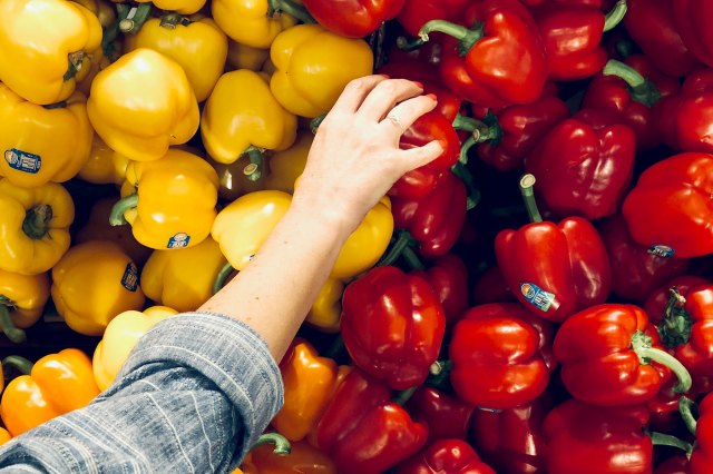 A woman picks up a red bell pepper from a selection of yellow and red bell peppers