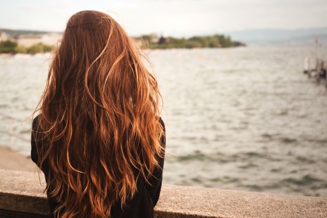 A woman with long red hair looks out at the ocean