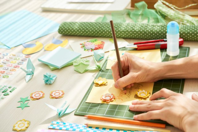 A close-up shot of a person creating a handmade greeting card while sitting at home, messy table surface