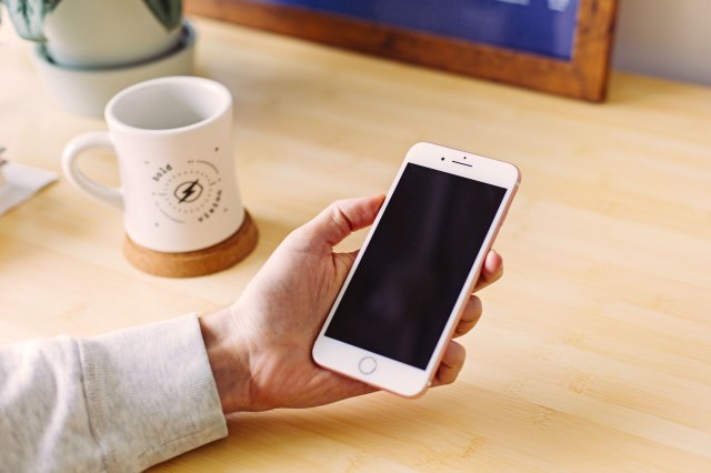 An image of a hand holding a phone with a desk in the background