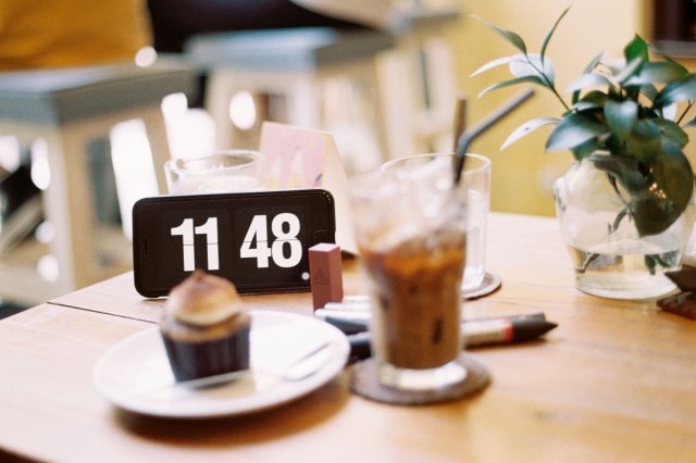 An image of a table with a cell phone, a plant, a cup, and a cupcake 