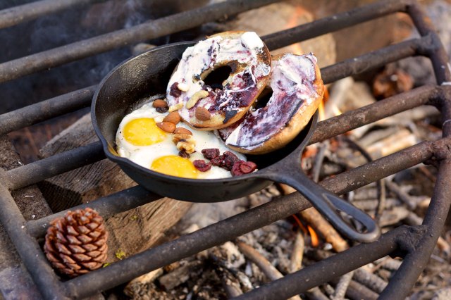 An image of a cast-iron pan on an outdoor grill with eggs and bagels in it