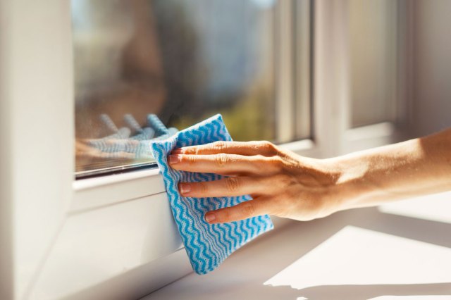 A close-up image of a person wiping a window with a blue and white cloth