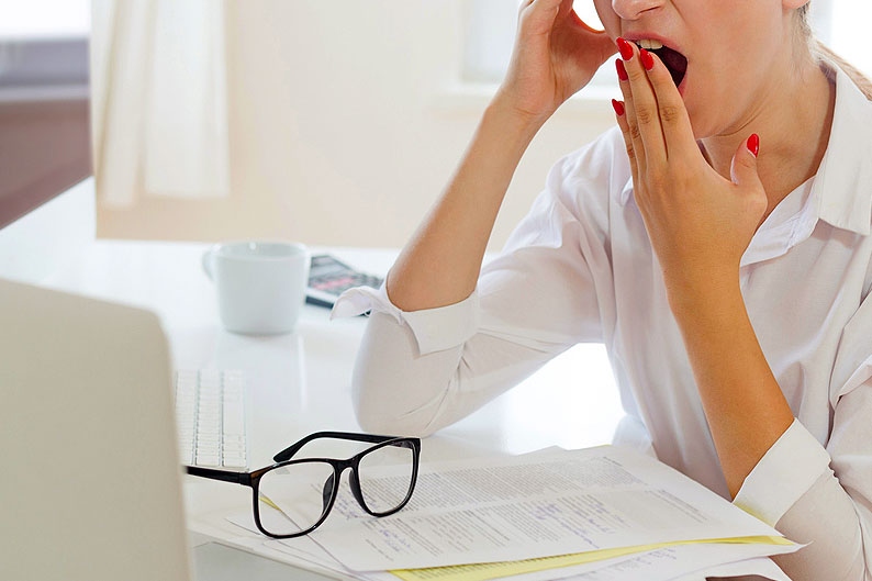 An image of a woman yawning while sitting at the computer