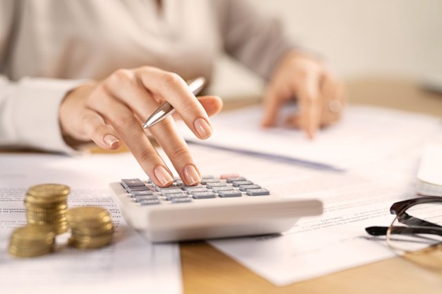 A close-up image of a woman touching a calculator on a desk