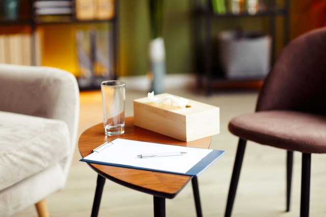A notepad, box of tissues, and a glass on a table in-between two chairs