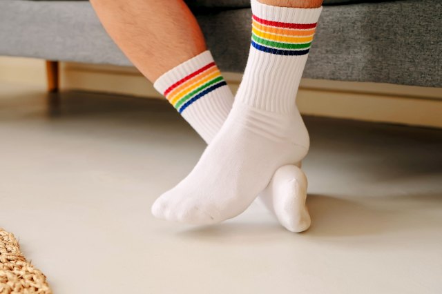 A person wearing a pair of white socks with rainbow trim crosses their ankles