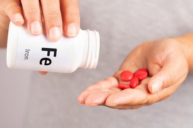 A close-up image of a person pouring pills into their hand from a white bottle