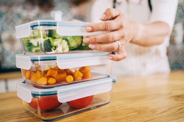 A close-up image of a woman stacking containers of vegetables