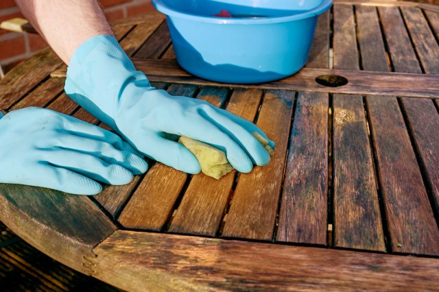 A person wearing gloves uses a sponge to scrub a wooden floor