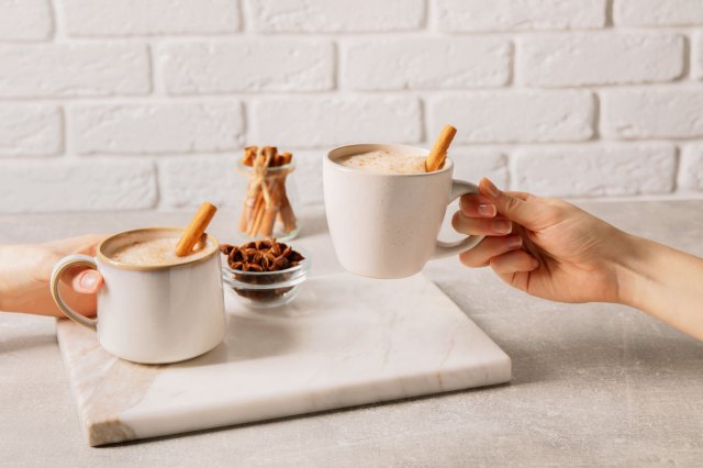A close-ip image of two people holding white coffee mugs with cinnamon sticks