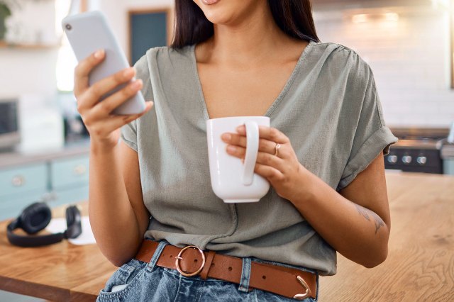 An image of a woman holding a mug while looking at her phone