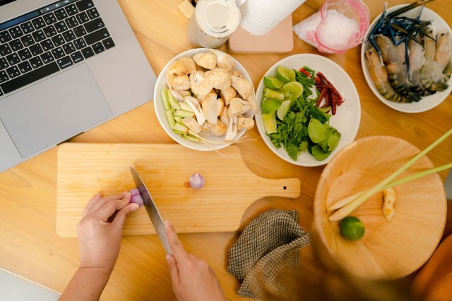 An aerial image of someone chopping food on a cutting board surrounded by small bowls of cut food and an open laptop