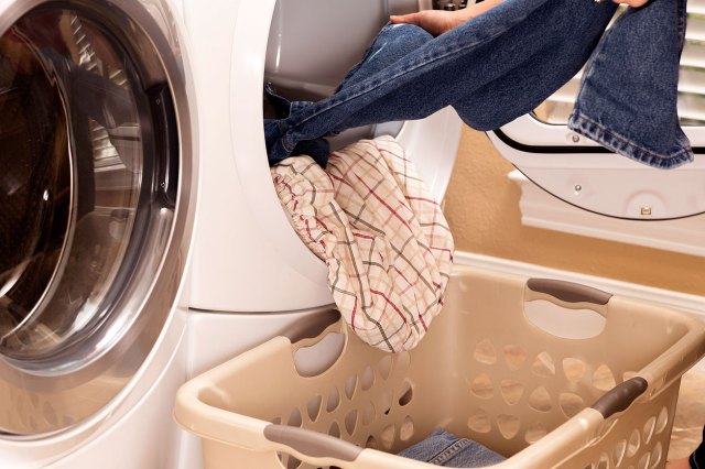 A person takes clothes out of a dryer and places them in a laundry hamper