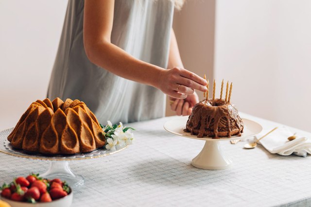 A close-up image of a woman putting candles into a cake on a dessert table
