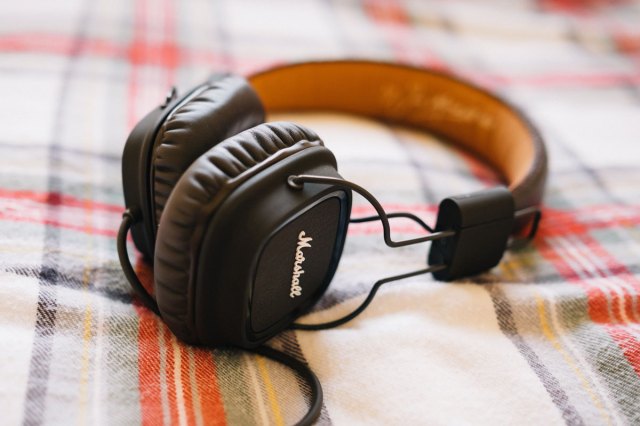 An image of large black headphones on a bed with flannel sheets