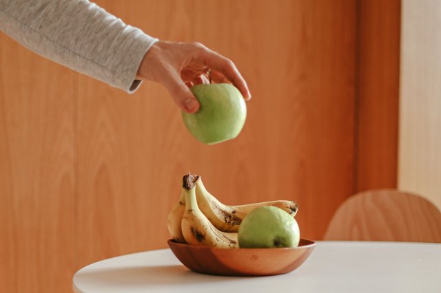 An image of a person putting a green apple into a bowl of fruit