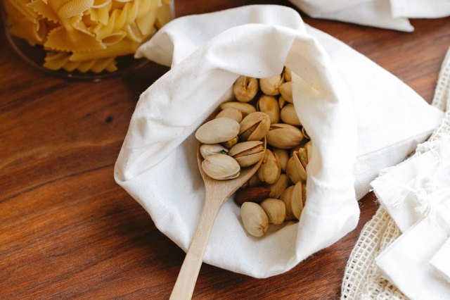 Wooden spoon in a white bag full of pistachios