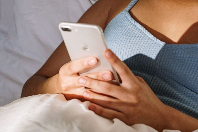 An image of a woman in bed holding a phone