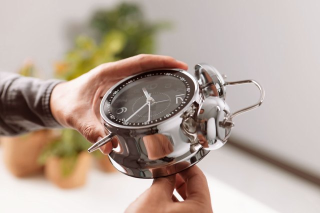 An image of hands holding a round silver alarm clock